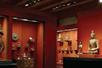 A room with dark red walls with several glass cabinets with pieces of art displayed in the at the Asian Art Museum.