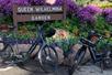 Two bikes parking in front of a small wooden sign that says "Queen Wilhelmina Garden" with purple flowers behind it.
