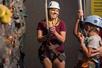 A woman in a hard hat and a harness standing next to a rock wall while watching a young boy start to climb up it at WonderWorks.