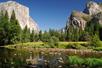 Wide shot of Yosemite National park from Merced River on a bright sunny day with a clear blue sky.