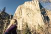 A hiker with long blonde hair looking up at trees and a mountain on the Total Yosemite Experience in San Francisco, California.
