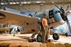 A replica of a Grumman with his shirt off standing next of a white and light blue F4F-3 Wildcat.