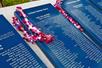 A row of black plaques with lists of names engraved on them with a pink and purple lei handing on the top left corner at the Pearl Harbor War Memorial.