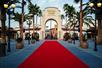 A red carpet with palm trees and light posts on both sides with the entrance to Universal Studios Hollywood at the far end.