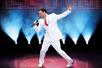 A man in a white suit with a bright red tie singing into a microphone with his other arm out at VEGAS! THE SHOW.