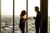 A man and a woman engage in conversation while holding drinks at Vue Orleans' 33rd Floor indoor Observation Deck, which offers floor-to-ceiling glass windows showcasing a stunning view of the New Orleans cityscape.