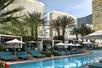 An outdoor swimming pool with luxurious lounge chairs and cabanas lining it with palm trees behind them at the Waldorf Astoria Las Vegas.