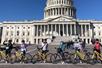 A group of tourist standing their their bikes and posing for a photo in front of the United States Capitol building on a sunny day.