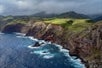 A cliffside shoreline with clouded mountains in the background on the West Maui Mountains and Molokai Helicopter Tour in Hawaii USA.