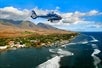 A helicopter flying by a coastal city with mountains in the background on the West Maui Mountains and Molokai Helicopter Tour in Hawaii USA.