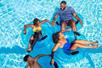 Four people in swim attire bond with each other as they relax on blue inflatable tubes on the lazy river, enjoying the sun and refreshing water.