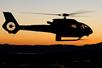 The silhouette of a Maverick helicopter flying with a bright orange sunset behind it near Las Vegas.