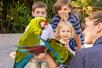 Three kids looking excitedly at a zoo keeper holding two bright green macaws on a sunny day at ZooTampa.