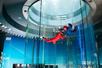 An instructor and a guest with their arms out flying high in the air in the flight tunnel at iFly.