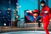 A guest in a blue suit flying in the air in the tunnel with an instructor in all red standing to her side at iFly.