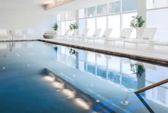 A relaxing indoor pool surrounded by large windows and sun loungers.