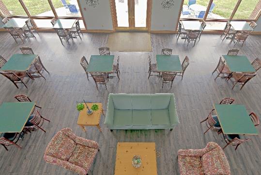 View looking down on a seating area with a couch, coffee table, and two arm chairs with square green dining tables around it.