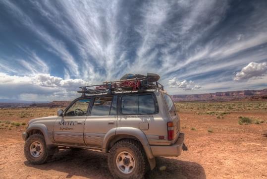 A silver NAVTEC SUV parked in Arches National Park with a dark cloudy sky moving overhead.