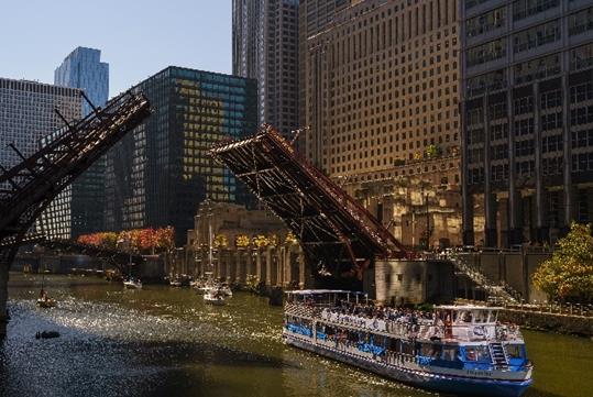 A tour boat sailing past one of Chicago's iconic bridges with city buildings in the background.