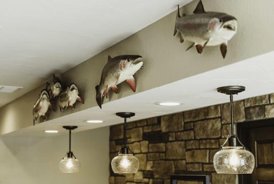 Three light fixtures with decorative fish art pieces mounted on the wall above them at the Bass Pro Shops Angler’s Lodge in Springfield.