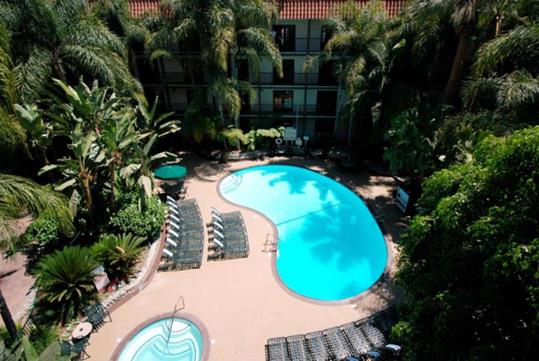 Aerial view of the resort and swimming pool surrounded by deep green trees on a sunny day.