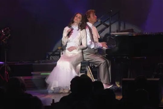 Sally Olson and Ned Mills siitng while singing together with live audiences.
