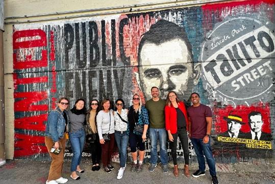 A tour group posed in front of a red and black mural where Dillinger took his last steps on the Chicago Crime Tours.