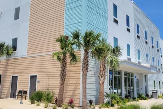 The Comfort Inn Miramar Beach-Destin exterior on a sunny day with small palm trees and ornamental grass in the landscaping.