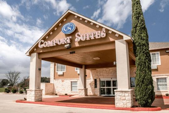 The front entrance of the Comfort Suites New Braunfels on a bright sunny day with clouds in the sky.