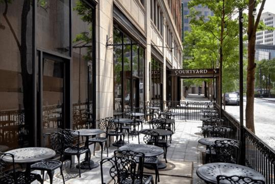 An outdoor patio with three rows of round iron tables with two chairs at them and the entrance to the Courtyard by Marriott Atlanta Downtown in the background.
