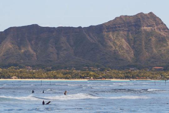 Wide shot of the Diamond Head cone seen from the coast off Waikiki with surfers in the lights blue water on a sunny day.