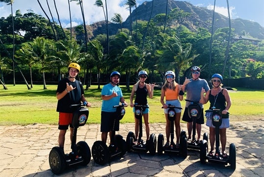 Group Posing on their segways in front of the Palm Trees and mountains on the Diamond Head Segway Tour, Honolulu Hawaii.