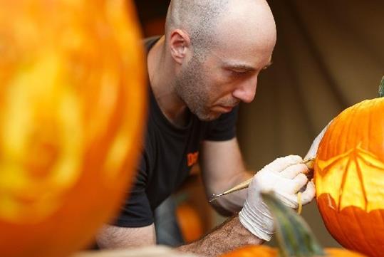 A bald man in a black shirt carving a bat into a pumpkin with another pumpkin in the foreground at Dollywood in Pigeon Forge, Tennessee, USA.