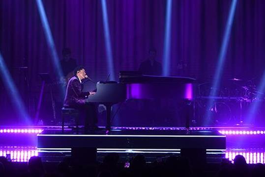 Donny Osmond singing on the stage while playing piano with purple lights shining behind him at Harrah’s in Las Vegas.
