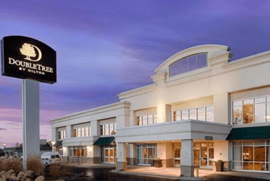 The white front exterior of the DoubleTree By Hilton with a covered entrance and a purple sky over head in Denver, Colorado.