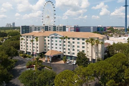 Wide shot the front exterior of the Fairfield Inn & Suites Orlando International Drive with trees around it and a ferris wheel in background.