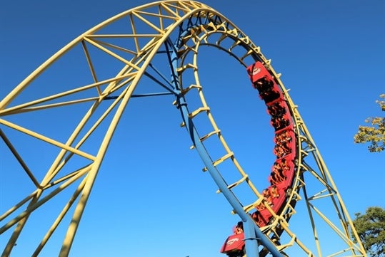 A roller coaster executing a loop, with riders visibly enjoying the thrill against a clear blue sky.