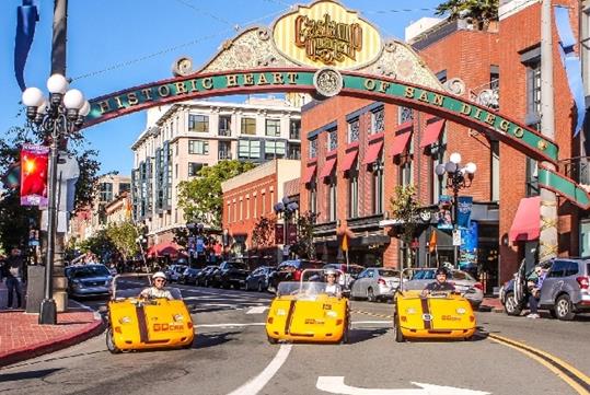 Three tourist in bright yellow GoCars parked under the iconic sign at the entrance to the Gaslamp Quarter on a sunny day in San Diego.