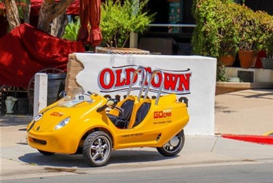 A bright yellow GoCar parked in front of a white and red sign saying "OLD TOWN" on a sunny day in San Diego.