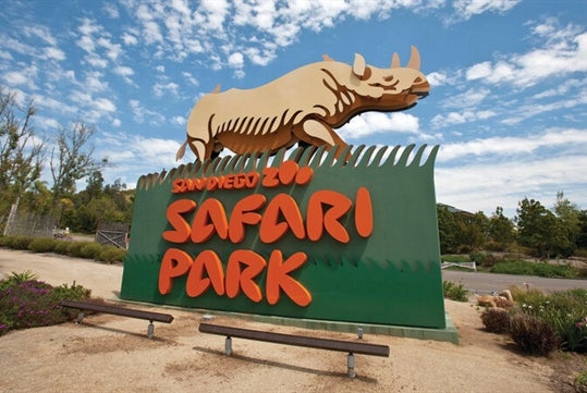 San Diego Safari Park Sign with lush green trees on the background set in cloudy blue skies with Go San Diego Explorer Pass.