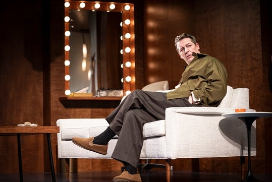 Sean Hayes sitting in a white chair on stage in Good Night, Oscar at the Belasco Theatre in NYC.