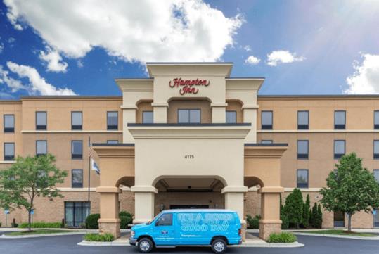 The front exterior of the Hampton Inn with a bright blue van parked out front in Minneapolis, Minnesota.