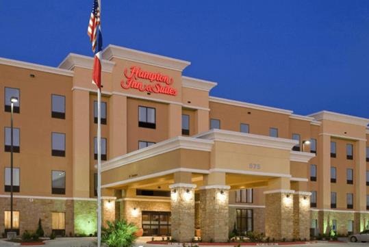 The front of the Hampton Inn & Suites New Braunfels with the exterior lights on at dusk with a clear sky over head.