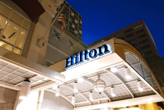 The front entrance to the Hilton Portland Downtown at night with lights illuminating the covered entrance and a glowing Hilton sign.