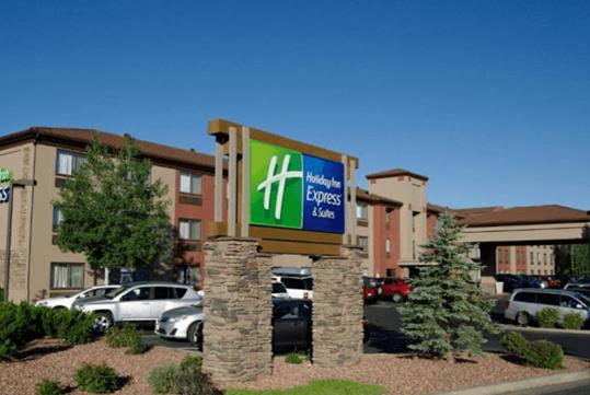The highway sign and front entrance of the Holiday Inn Express Grand Canyon with a parking lot full of car on a sunny day.