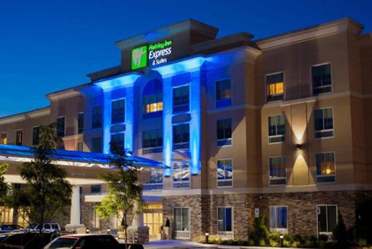 The front exterior of the Holiday Inn Express & Suites at night with blue lights illuminating the center.