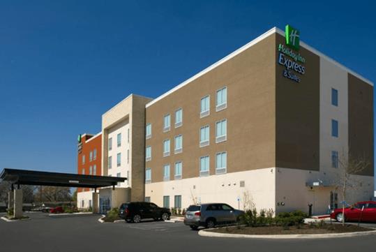 The exterior of the Holiday Inn Express & Suites New Braunfels with cars parking lot and a covered entrance on a sunny day.