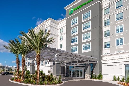 The front exterior and covered entrance of the Holiday Inn & Suites Orlando International Drive South with beautiful landscaping around the entrance.