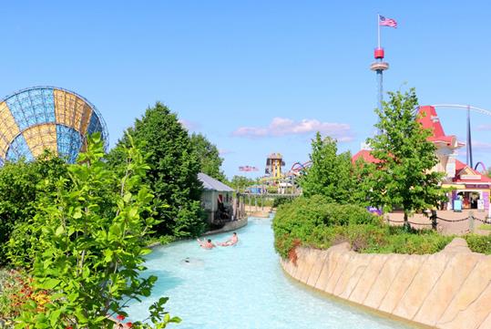 The Castaway Creek lazy river surrounded by greenery and colorful amusement rides under a clear blue sky.