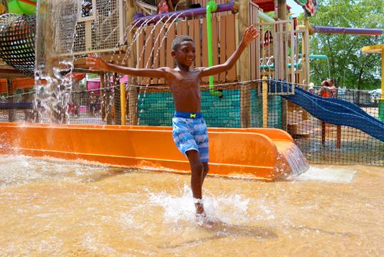 A young boy with his hands raised, joyfully plays with the water at Tiki Island, a part of Caribbean Cove at Hurricane Harbor Rockford.